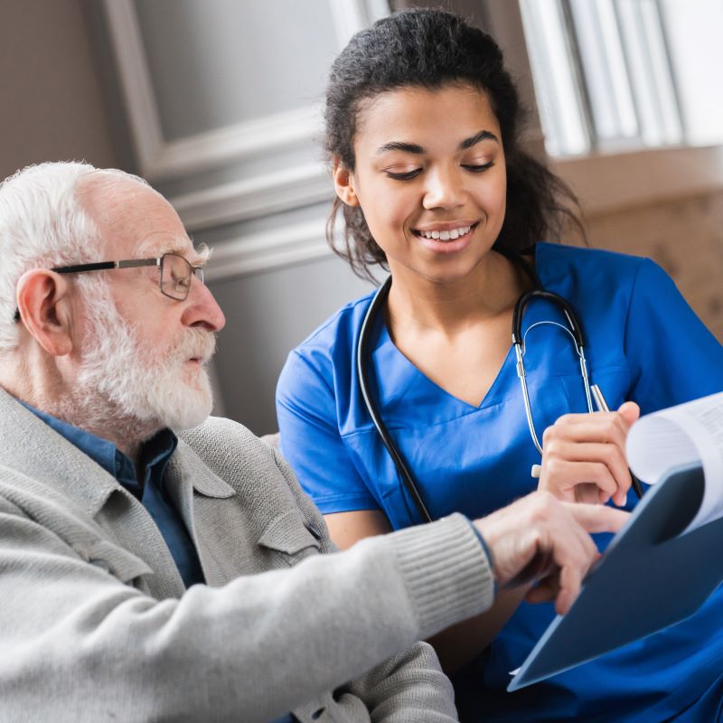 Older man talking to nurse with clipboard.