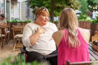 Mother with disability in wheelchair talking to her daughter while sitting at the table in cafe in the street