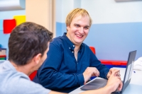 young adult man with IDD on a laptop computer with a caregiver/teacher