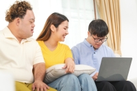 Three people sit on a couch, two young men and a young woman, sit on a laptop watching what's occurring on screen.